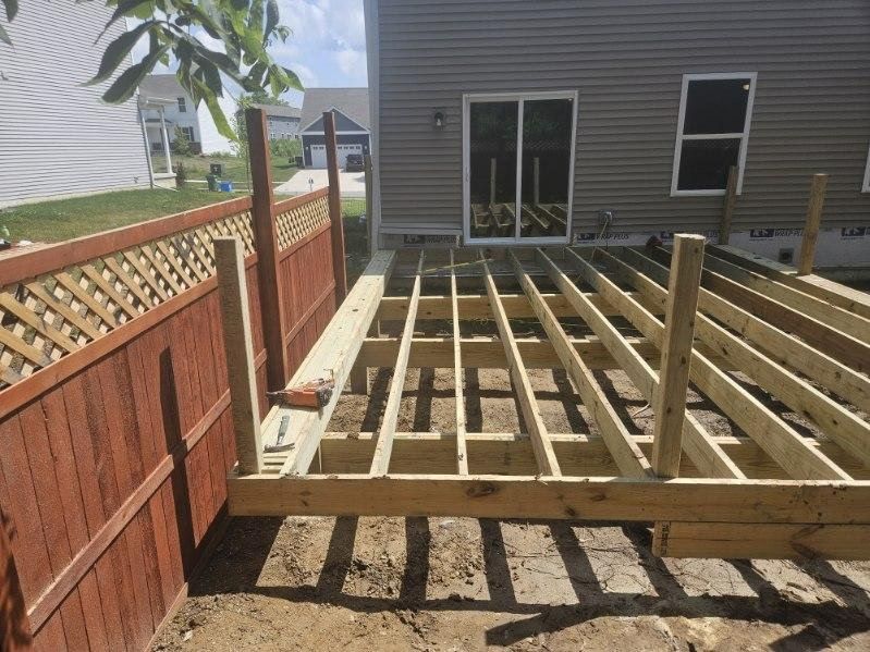 Wooden deck frame under construction next to a fence and house with sliding glass door.