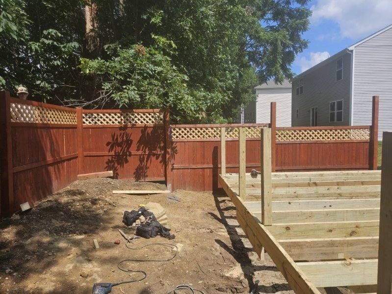 Backyard with a wooden fence and stairs under construction; dark reddish-brown fence, unfinished wood stairs and posts.