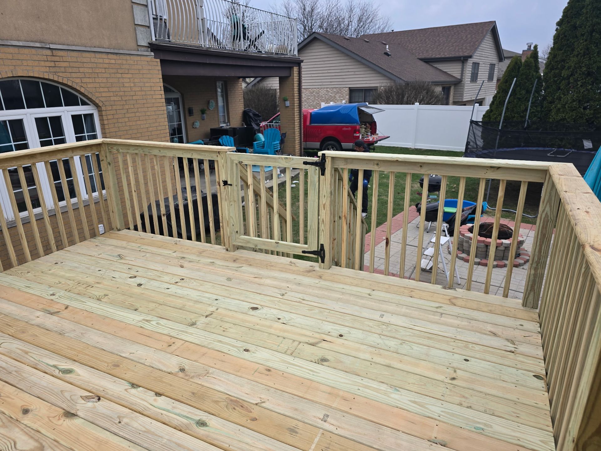Wooden deck with a gate and railing, leading to a backyard with a fire pit.