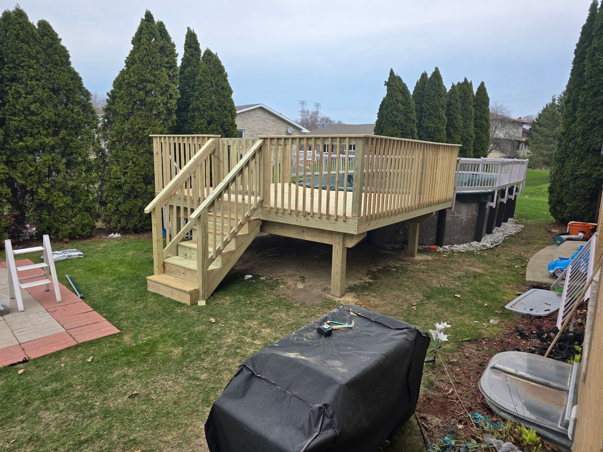 Wooden deck with stairs in a backyard with trees and a covered grill.