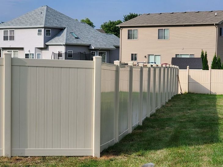Tan vinyl fence in a backyard setting with houses in the background.