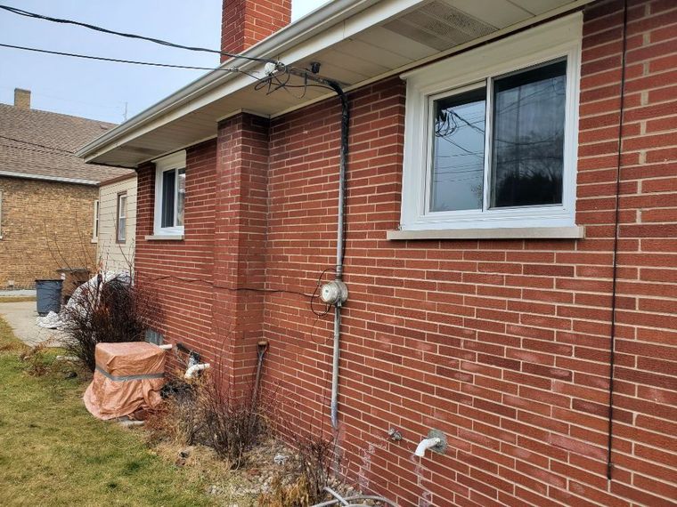 Construction worker in orange vest and blue hard hat inspecting window, holding tablet.