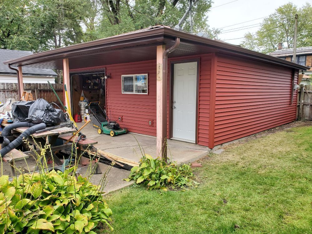 Red shed with a covered porch, white door, and open garage, surrounded by grass.