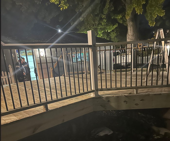 Wooden deck with black railing at night; house in background.