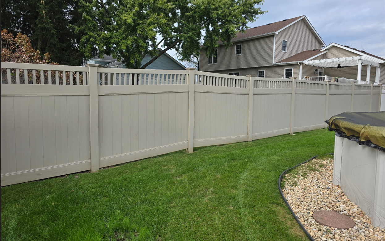 Tan vinyl fence along green lawn, houses in background.