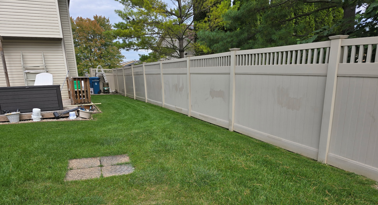 A green lawn with a gray fence along the side of a house on a sunny day.