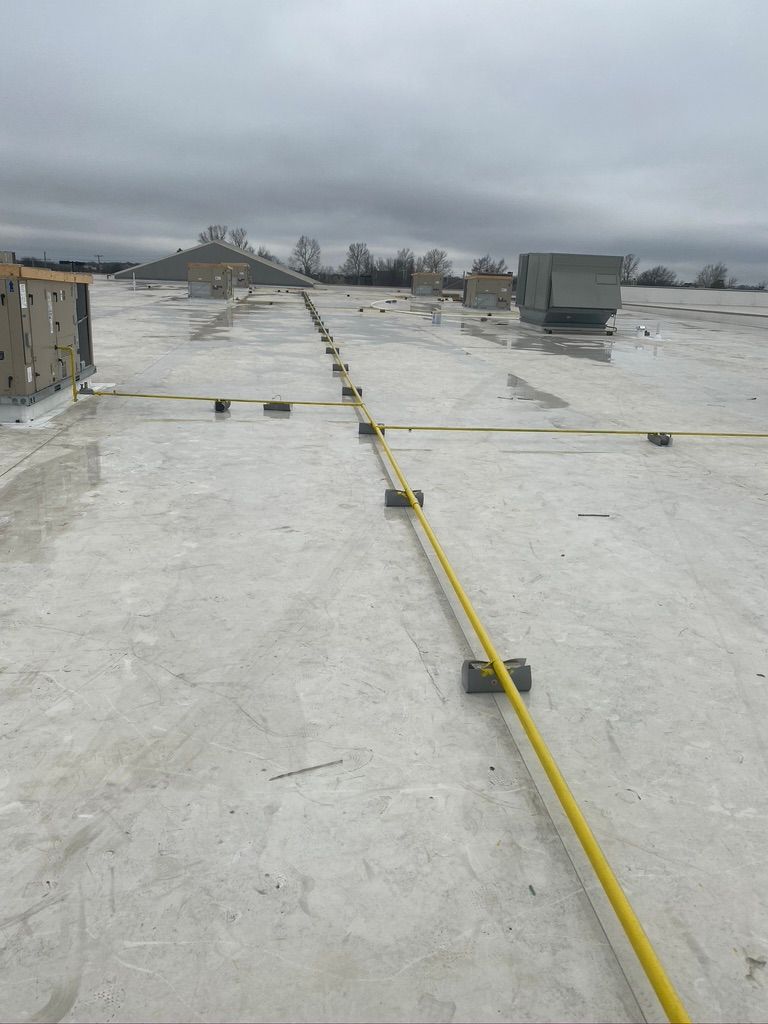 Cowboys Plumbing - Flat commercial rooftop with yellow safety line. Gray, cloudy sky.