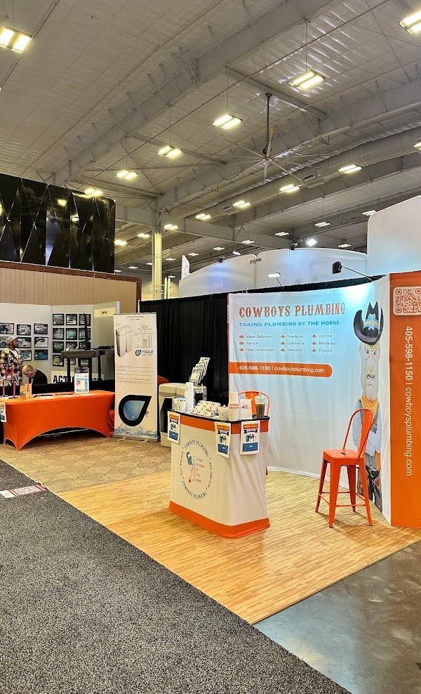 Cowboys Plumbing - Trade show booth, white and orange, promoting plumbing services. Signage, information, small stool.