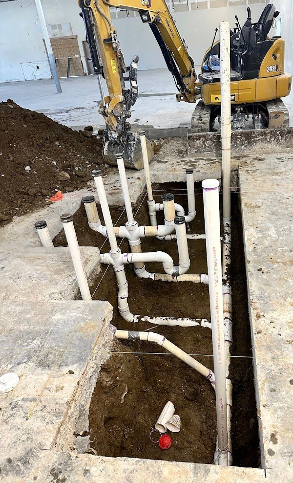 Cowboys Plumbing - Excavator digging around white PVC pipes in a trench. Construction site.