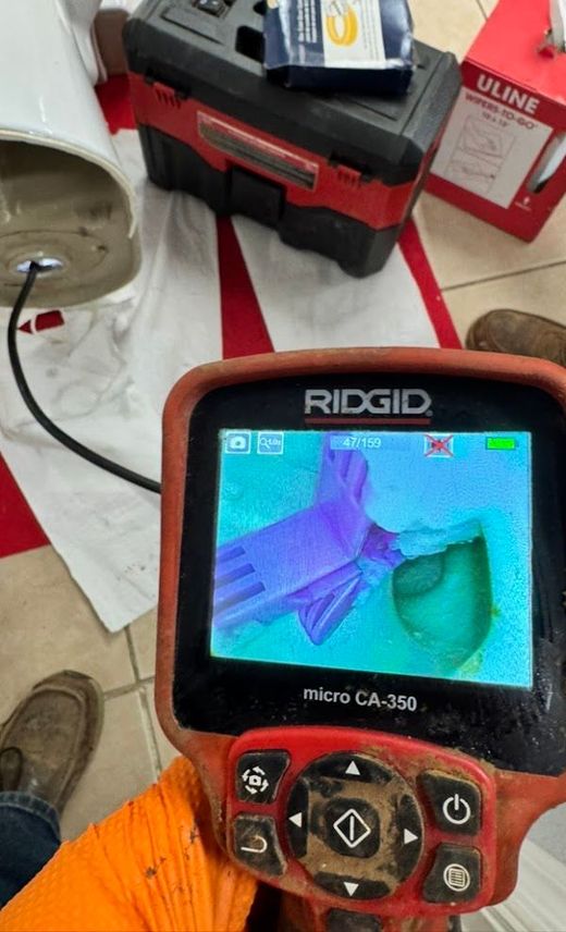 A worker uses a drain inspection camera. A camera monitor is on a tripod displaying the interior of a drain.