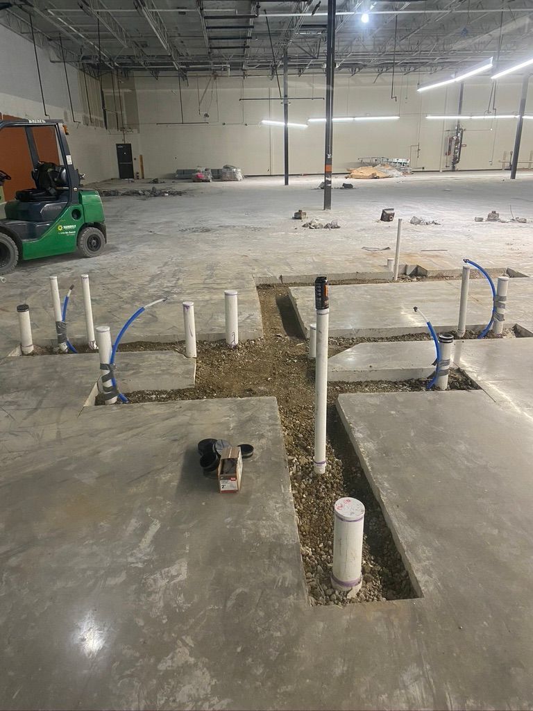 Cowboys Plumbing - Construction site showing plumbing pipes in concrete floor. A forklift sits in the background.