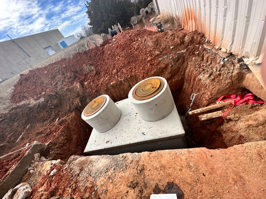 Cowboys Plumbing - Two concrete septic tank lids in an open excavation. Red soil, white wall, blue sky.