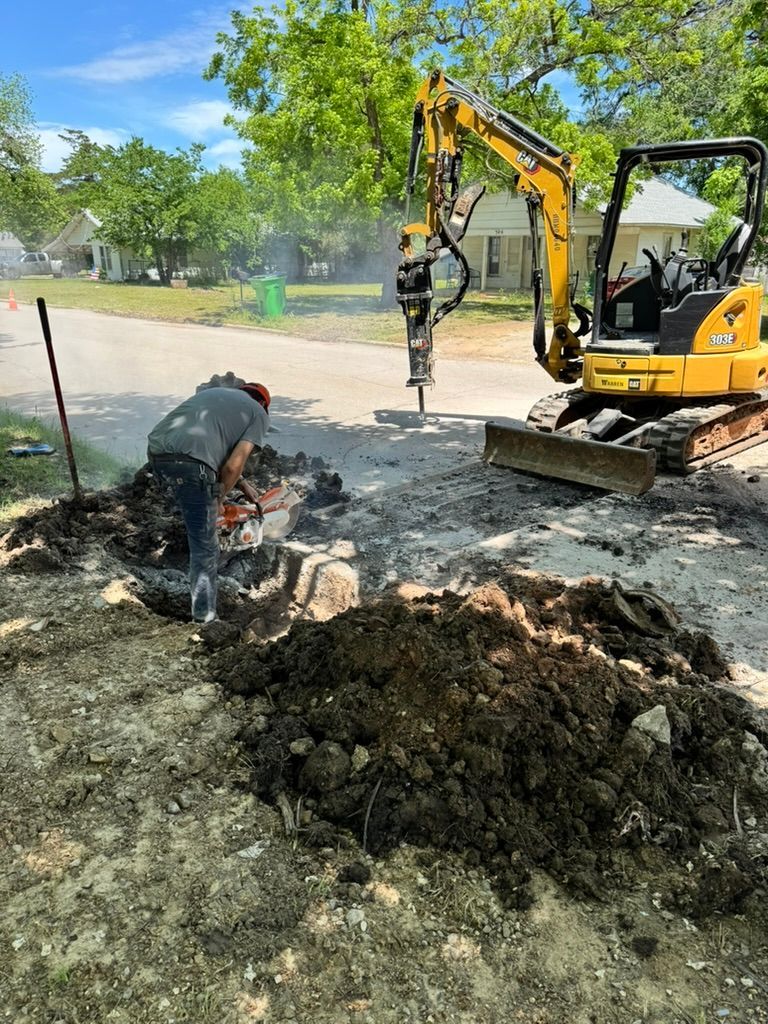 Cowboys Plumbing - Cowboys Plumbing - Construction worker using a chainsaw near a mini-excavator breaking ground on a street.