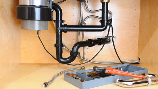 Plumbing under a kitchen sink: garbage disposal, pipes, tools in a cabinet.