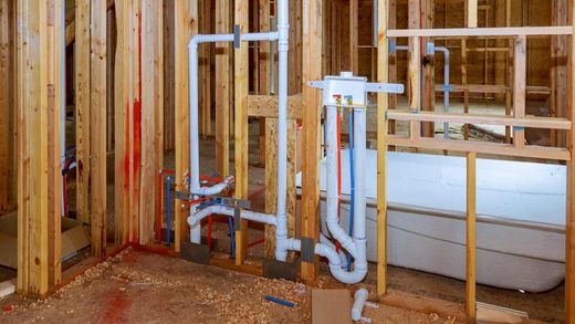 Bathroom under construction, with wooden framing, white pipes, and a bathtub.