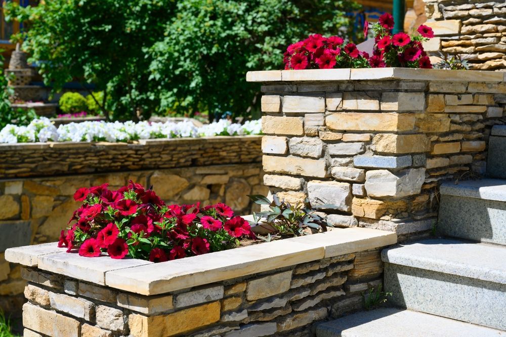 A stone wall with a planter filled with red flowers.