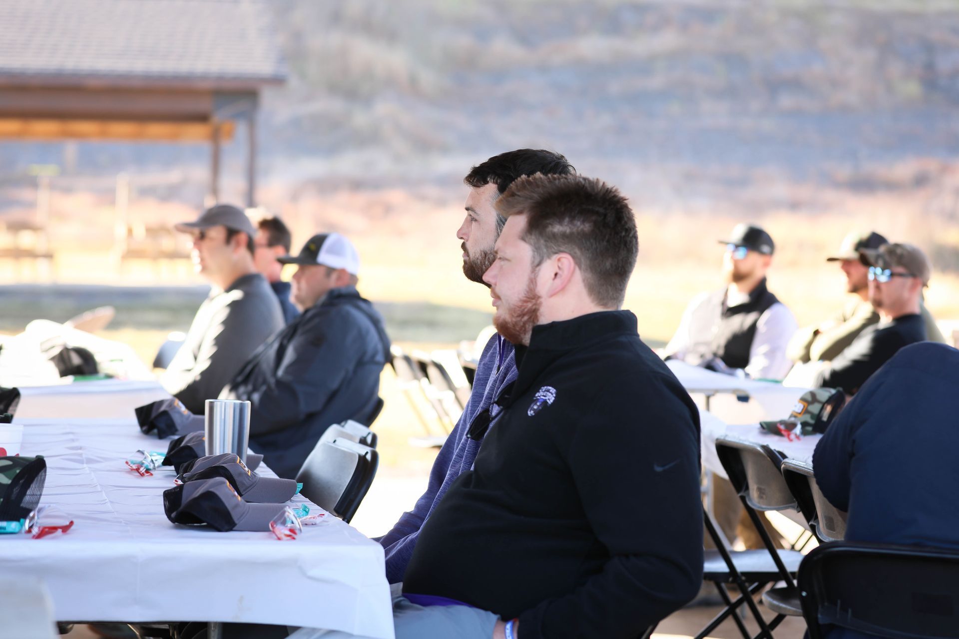 A group of men are sitting at tables outside.