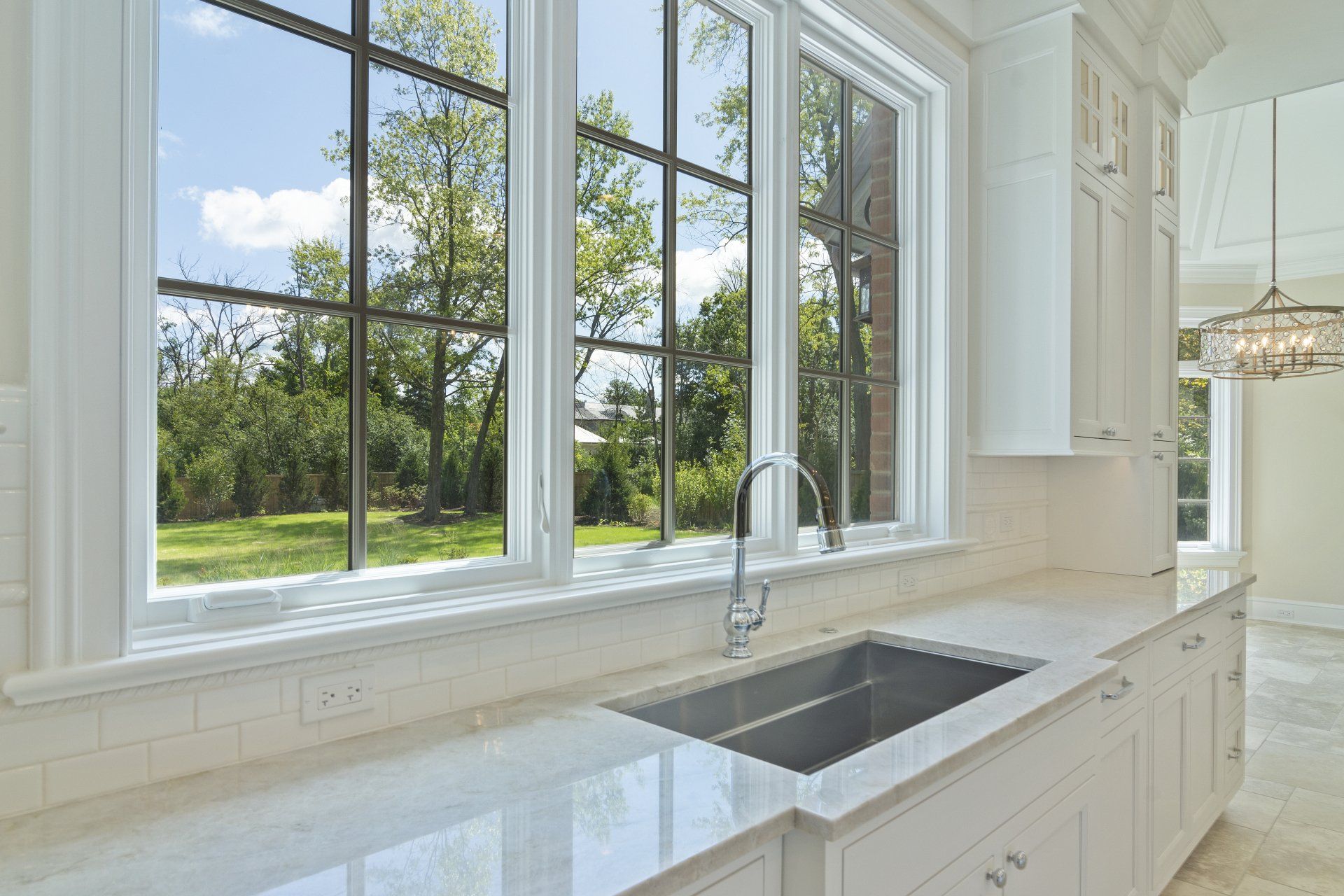 A kitchen with a sink and two windows with trees in the background.