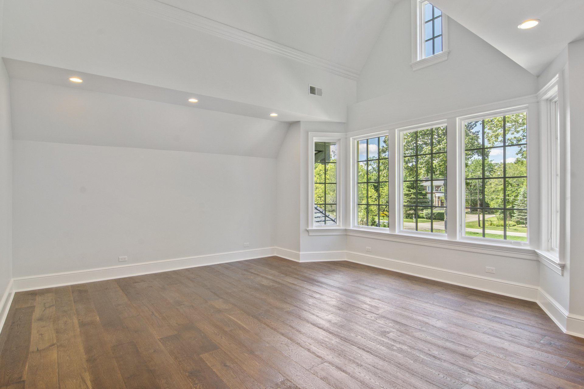 An empty room with hardwood floors and lots of windows.