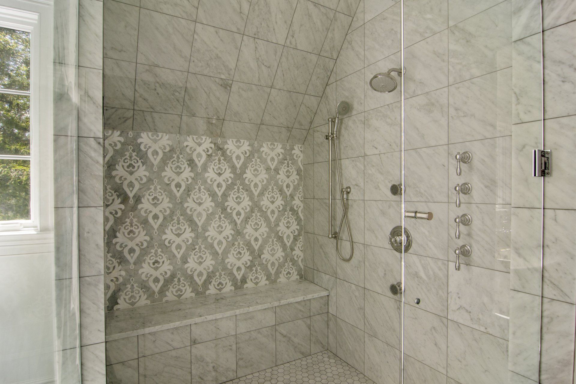 A bathroom with a walk in shower with a bench and a window.