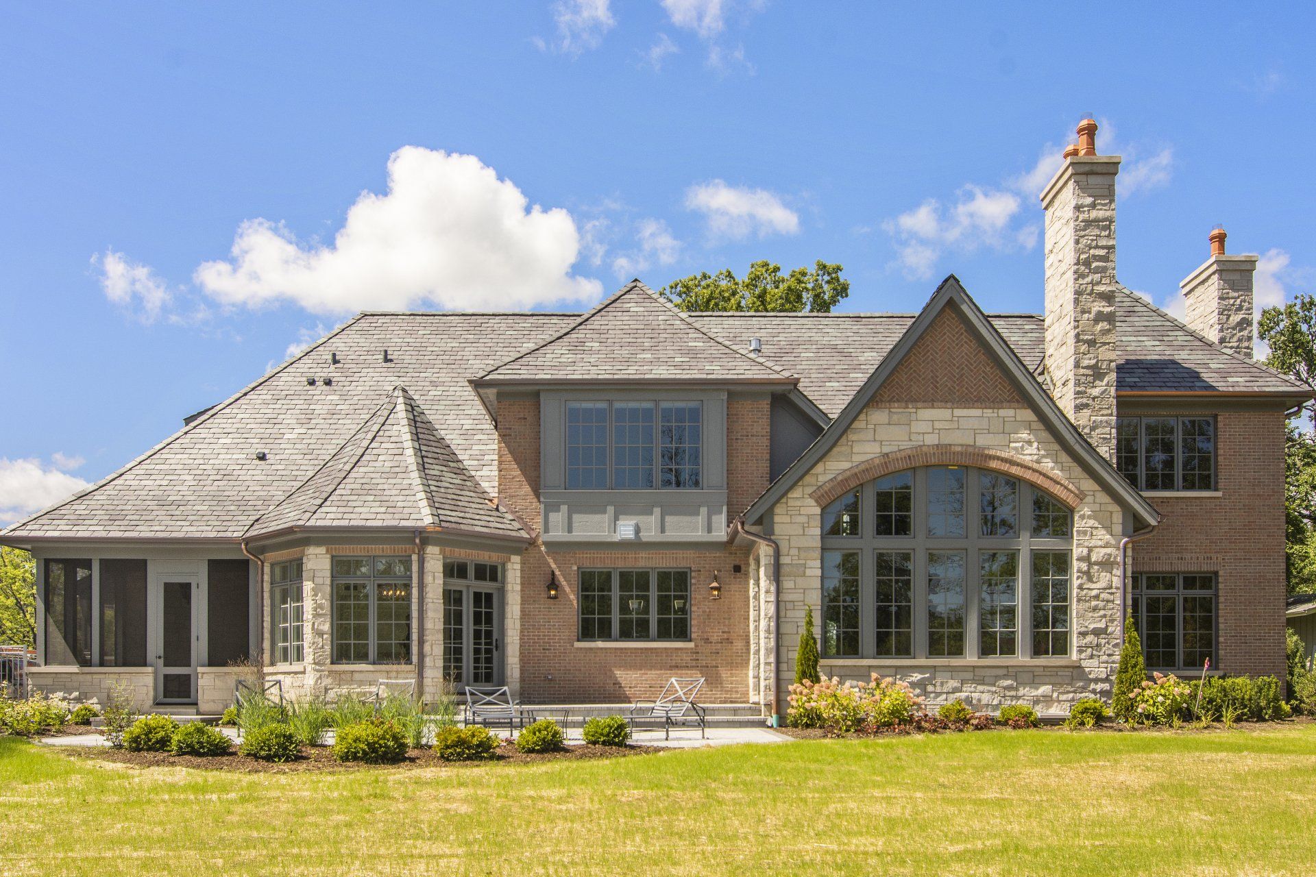 A large brick house with a gray roof is sitting on top of a lush green field.