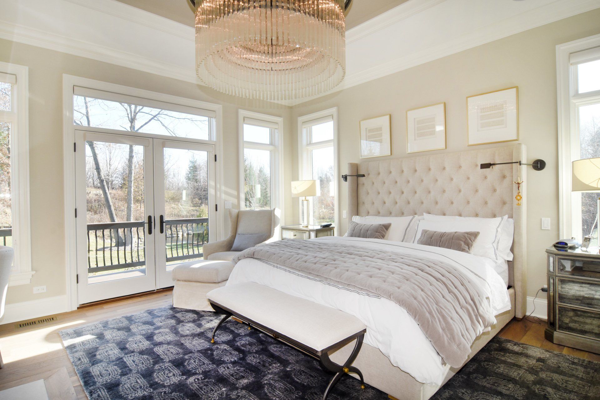 A bedroom with a large bed , a chandelier , a chair and a rug.