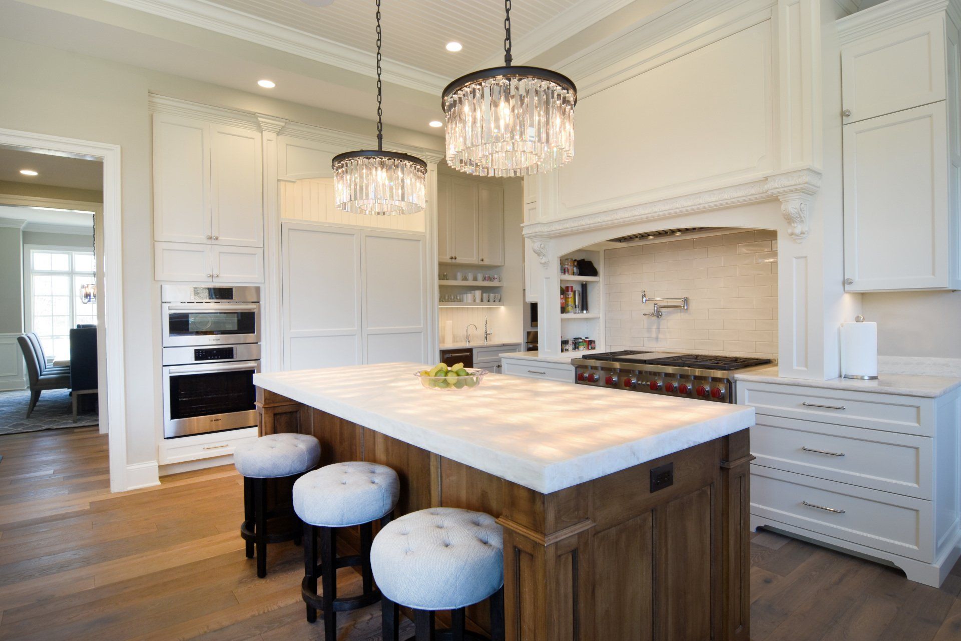 A kitchen with a large island and stools and a chandelier hanging from the ceiling.
