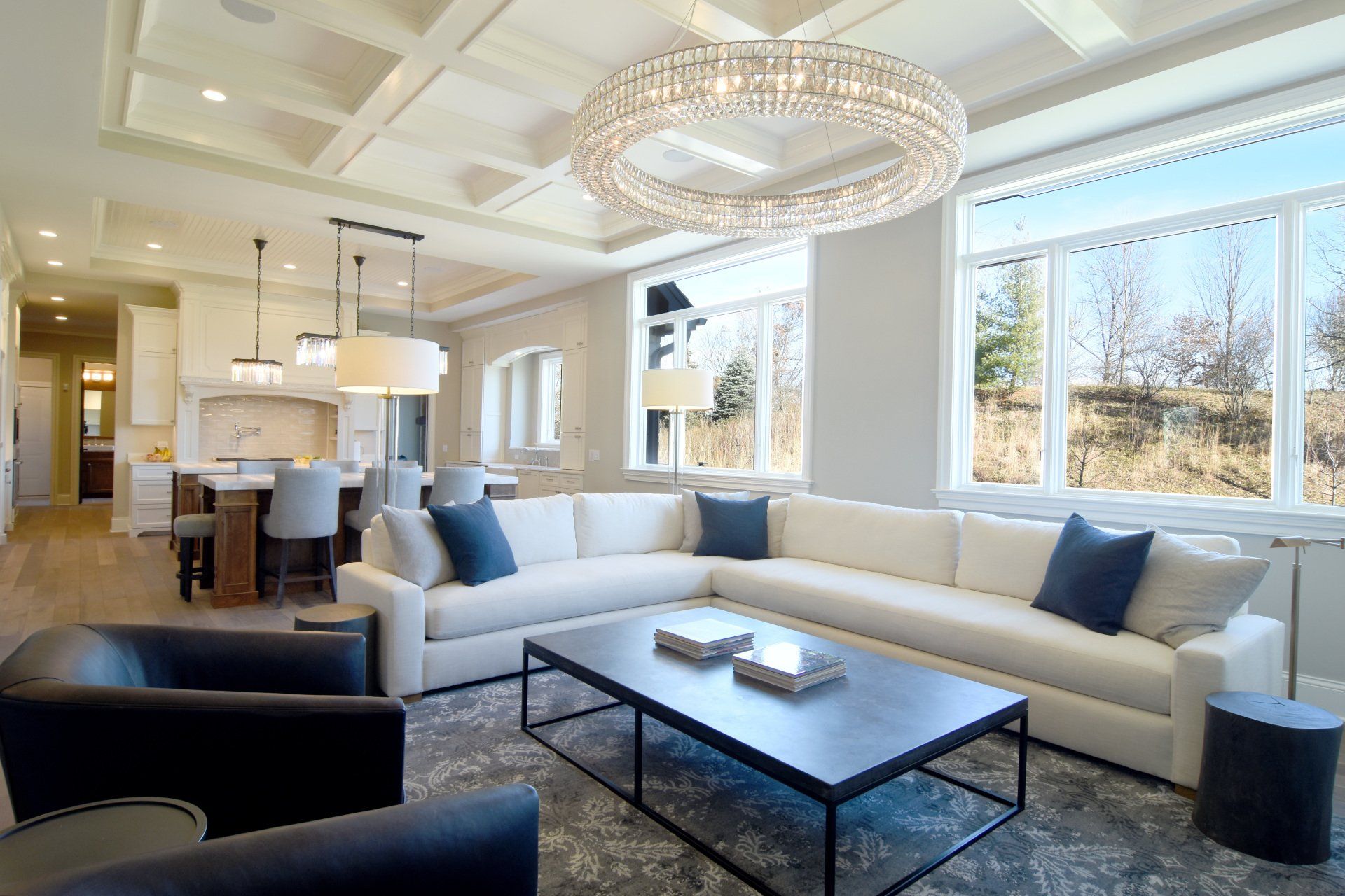 A living room with a large sectional couch , two chairs , a coffee table and a chandelier.