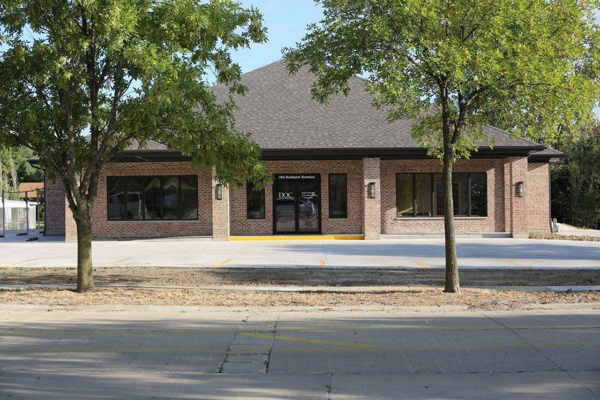 A brick building with a black roof and trees in front of it