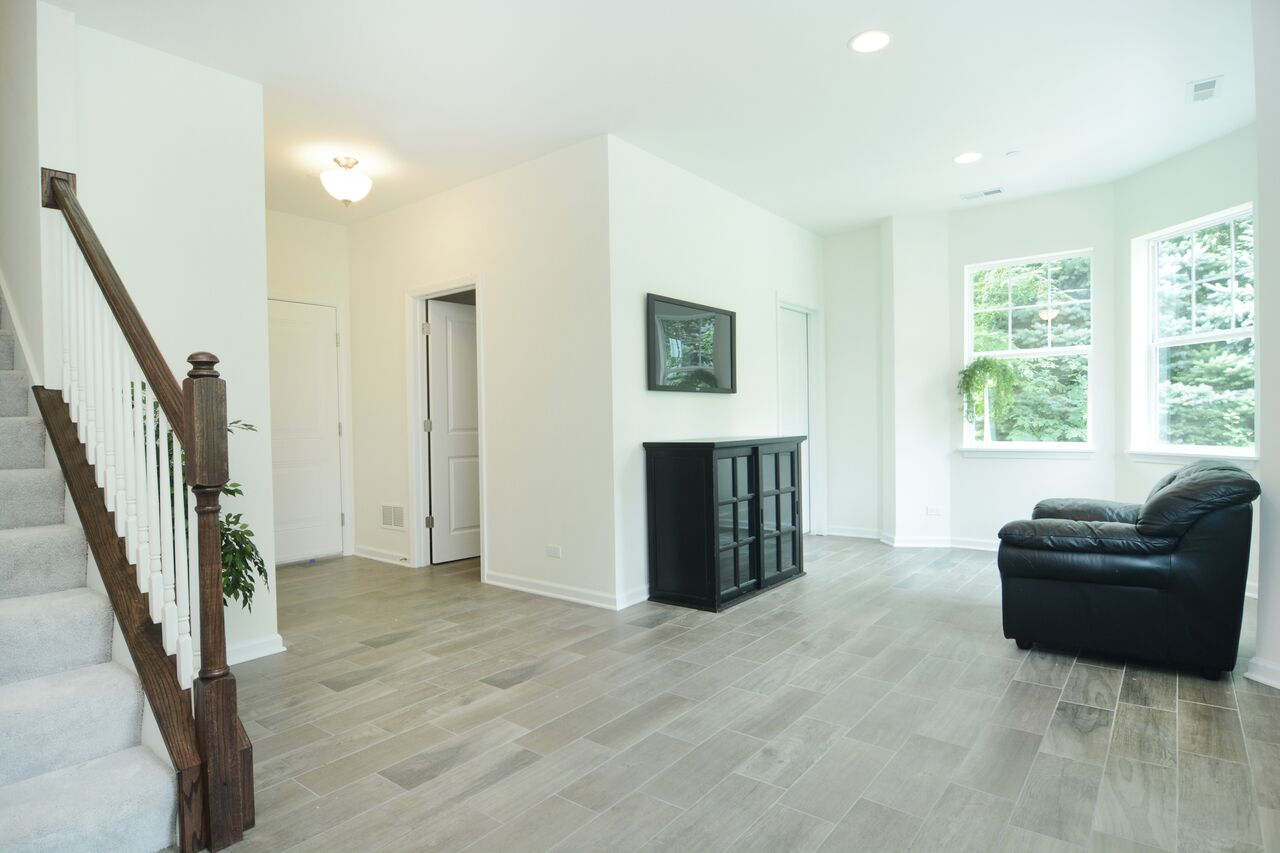 A living room with hardwood floors , a staircase , a chair and a dresser.