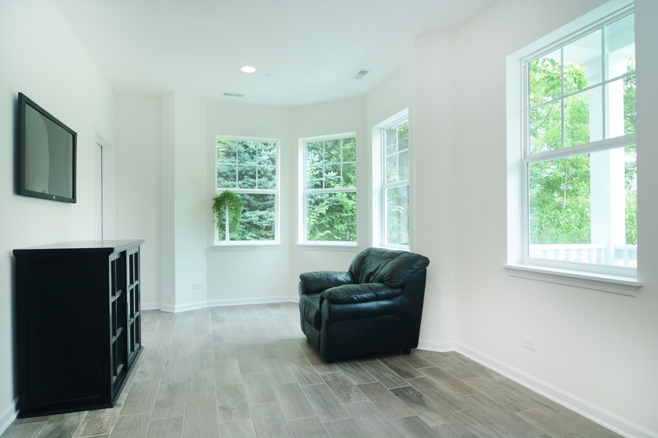 A living room with a black chair , a television , and two windows.