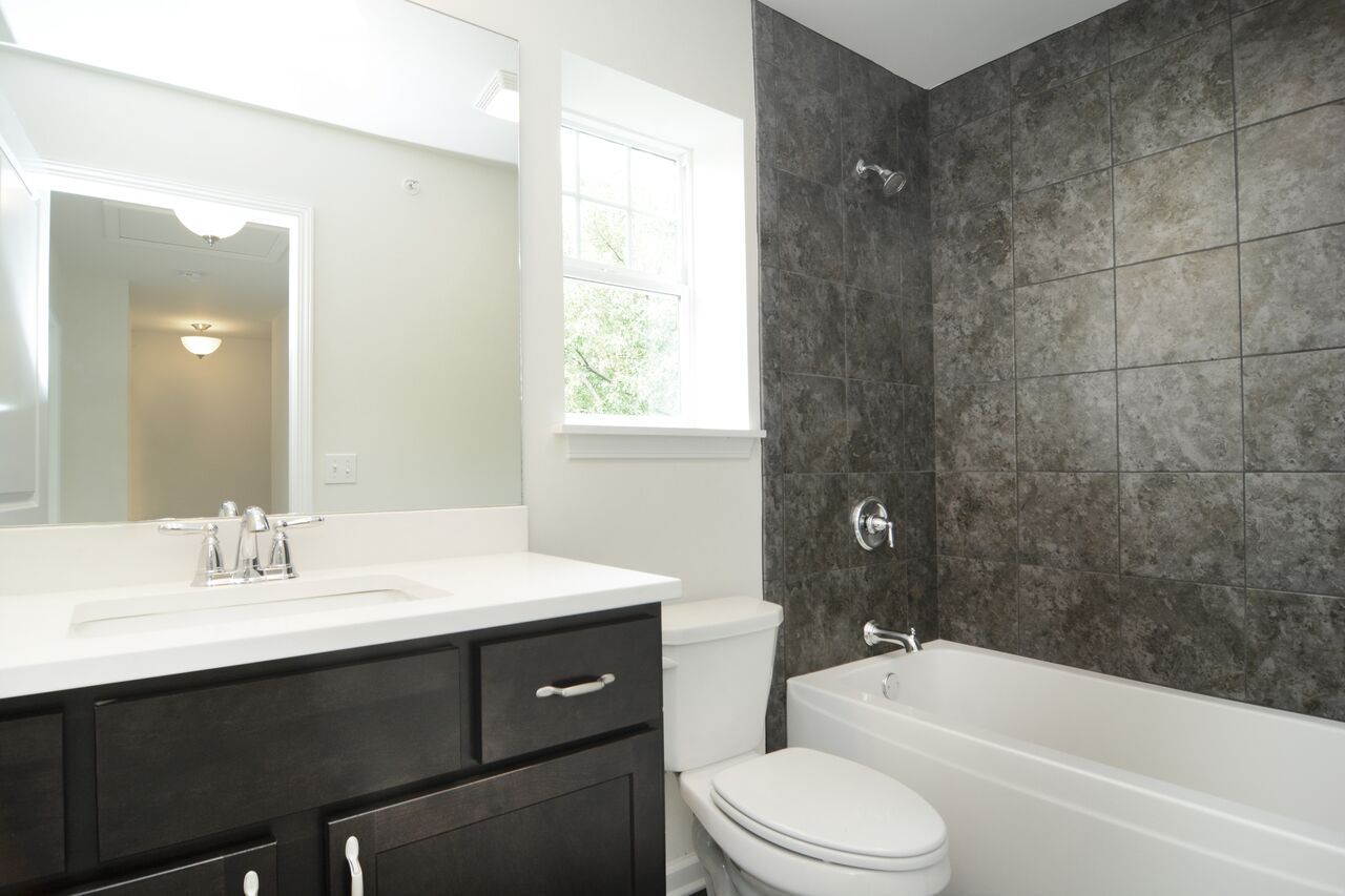 A bathroom with a toilet , sink , tub and mirror.