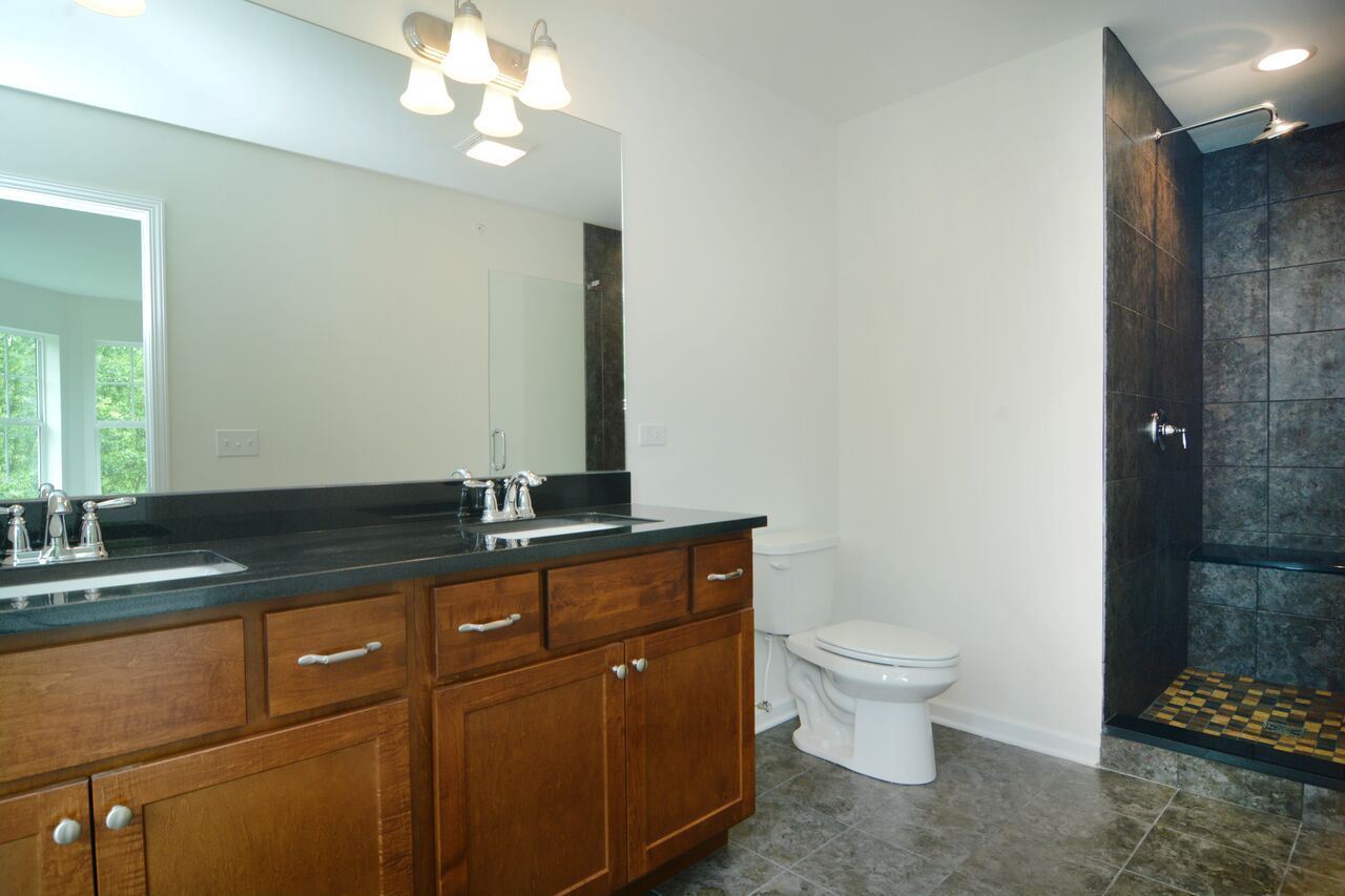 A bathroom with two sinks , a toilet , and a walk in shower.