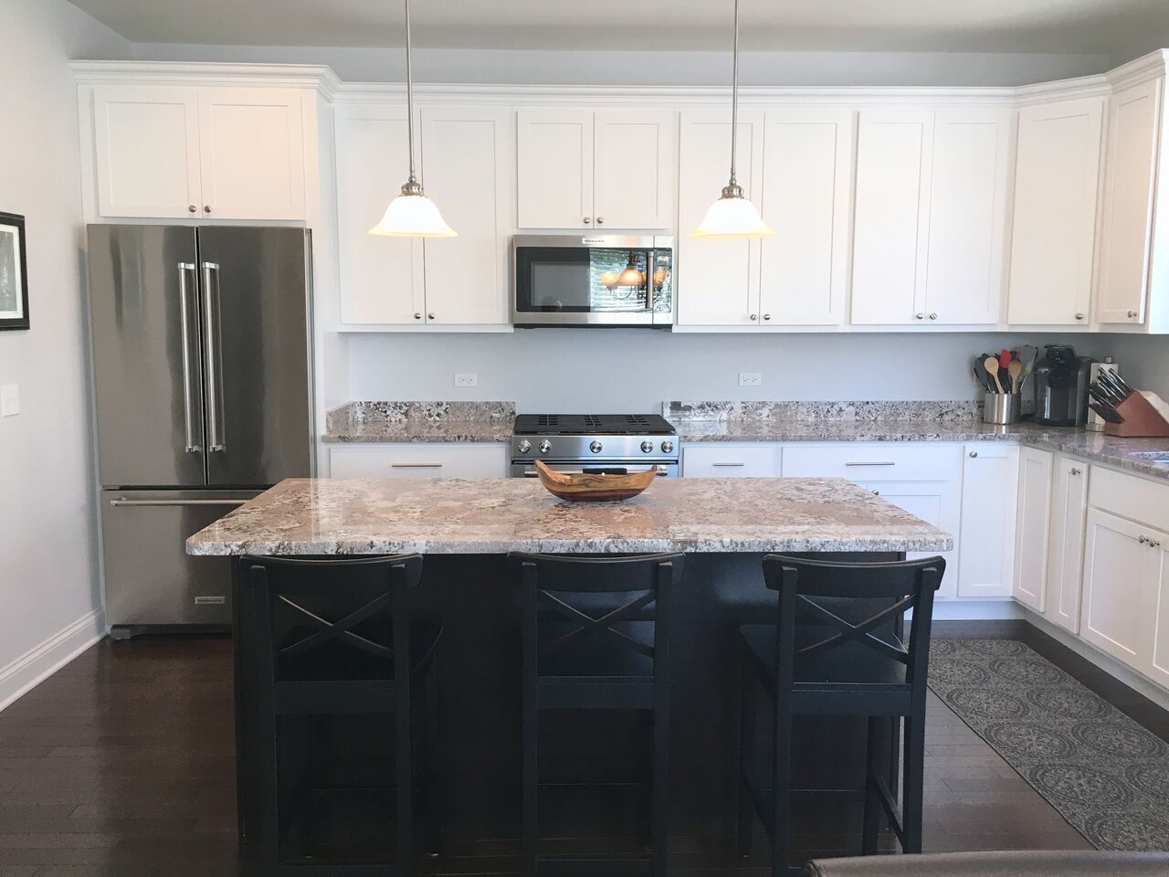 A kitchen with white cabinets , granite counter tops , stainless steel appliances and a large island.