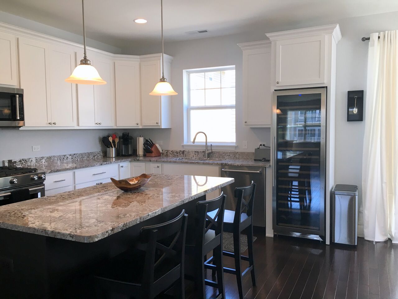 A kitchen with white cabinets , granite counter tops , stainless steel appliances and a large island.