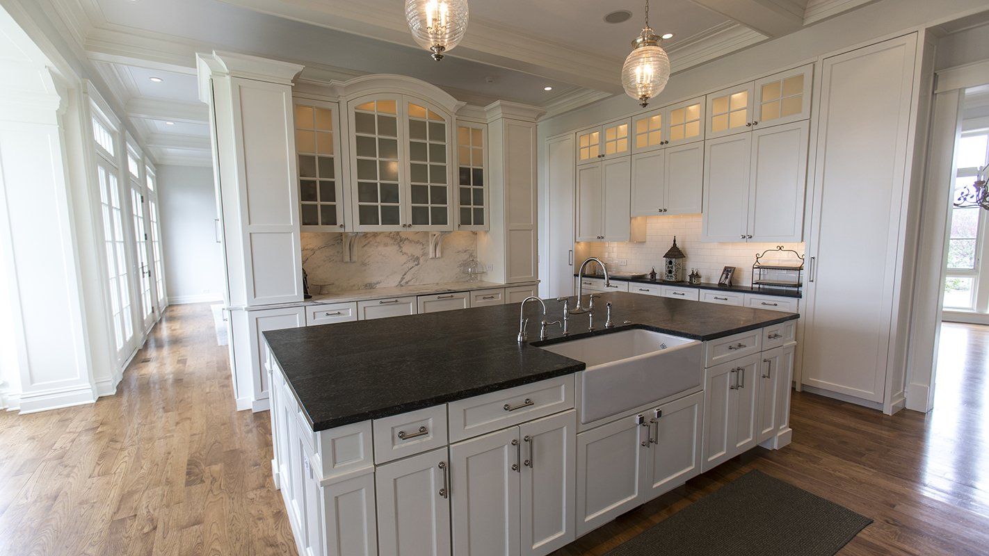 A kitchen with white cabinets , black counter tops , and a large island.