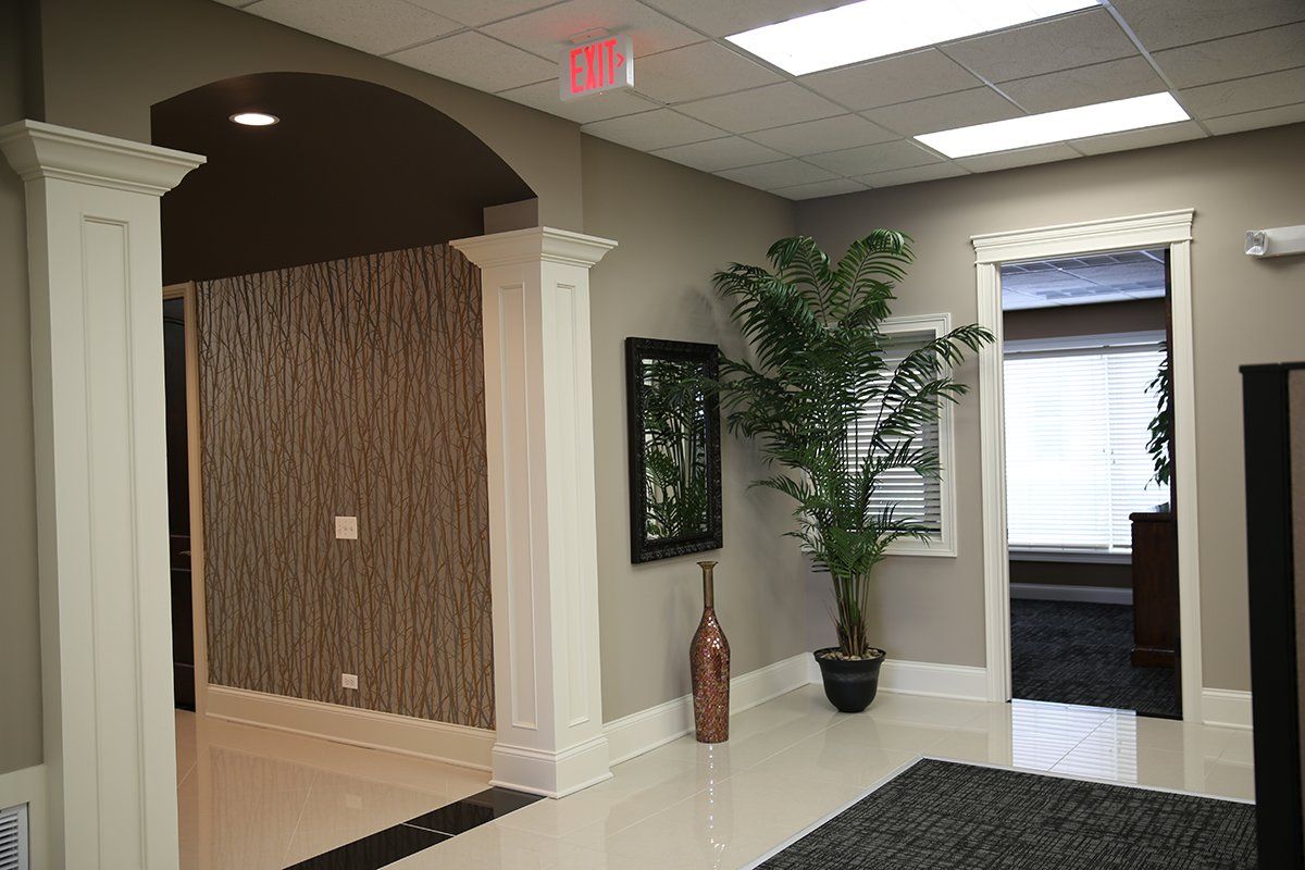 A hallway with a potted plant and a red exit sign on the ceiling.