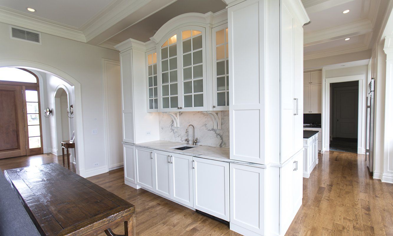 A kitchen with white cabinets and hardwood floors in a house.