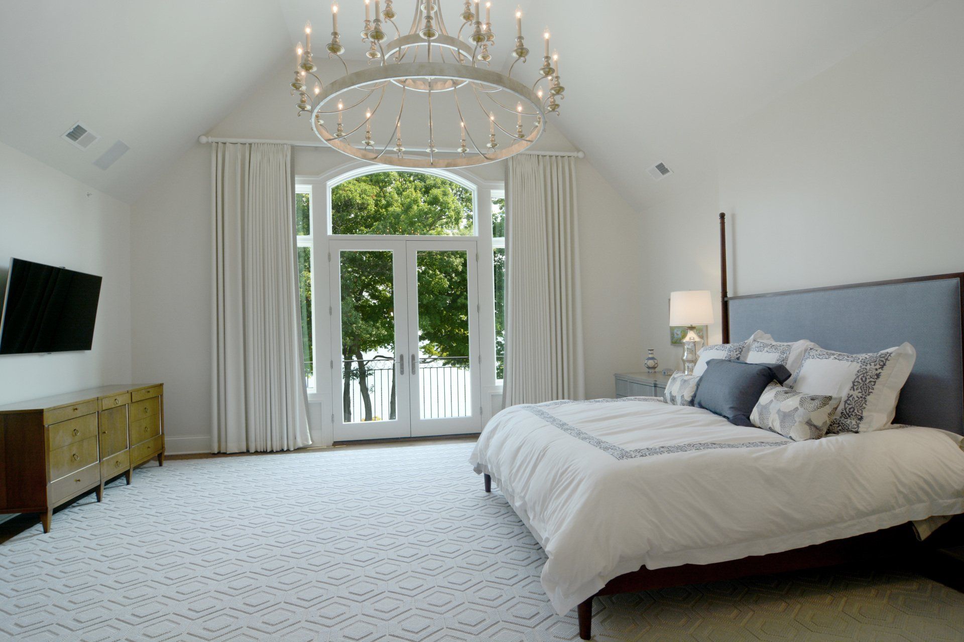 A bedroom with a large bed , television , and chandelier.