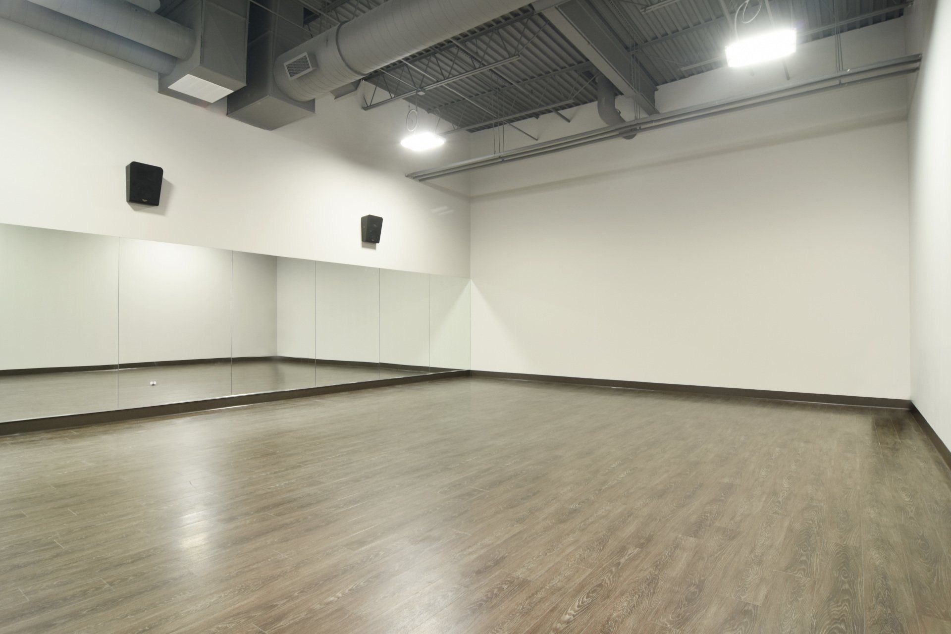 An empty dance studio with a wooden floor and mirrors.