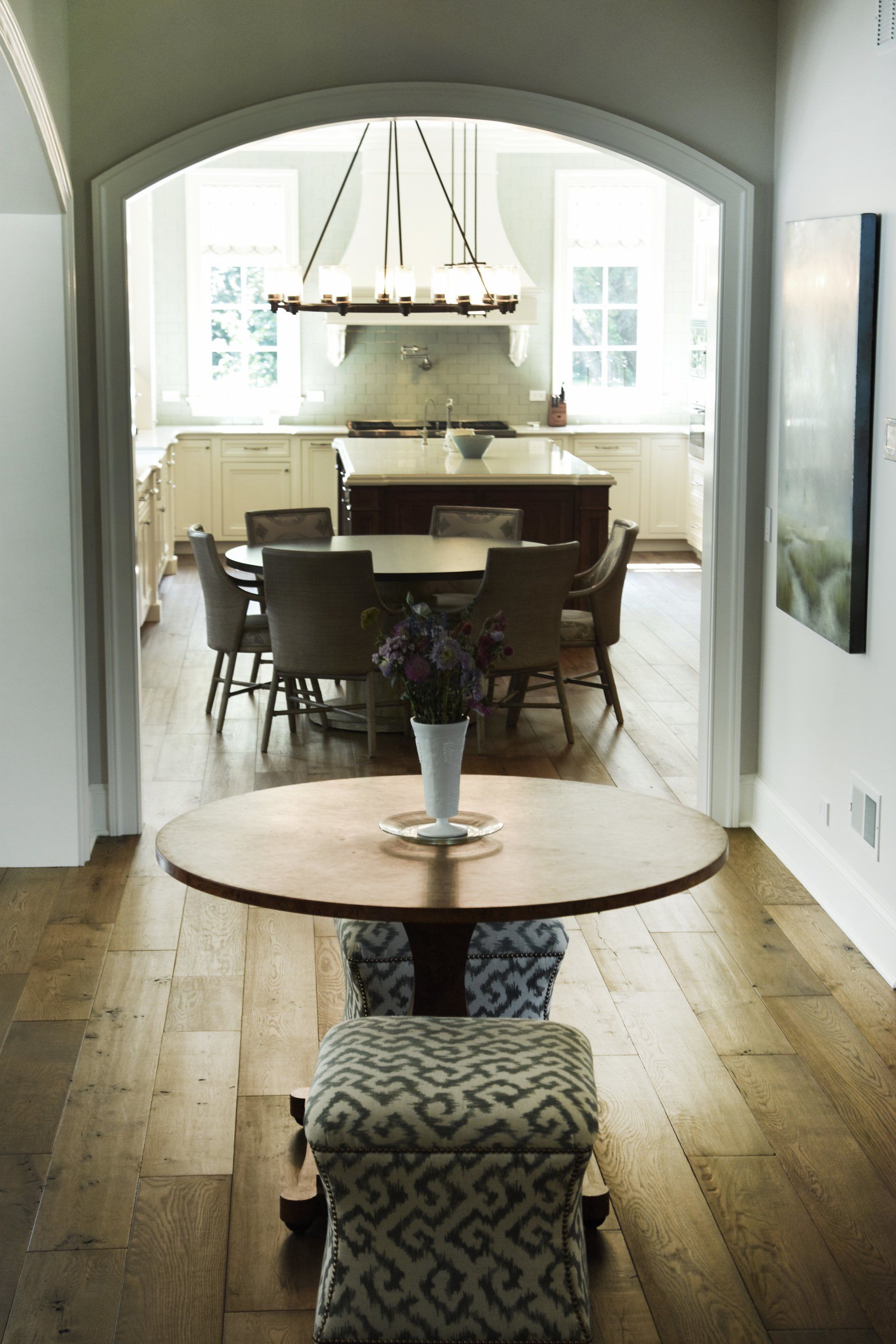 A table with a vase of flowers on it in a hallway leading to a dining room.