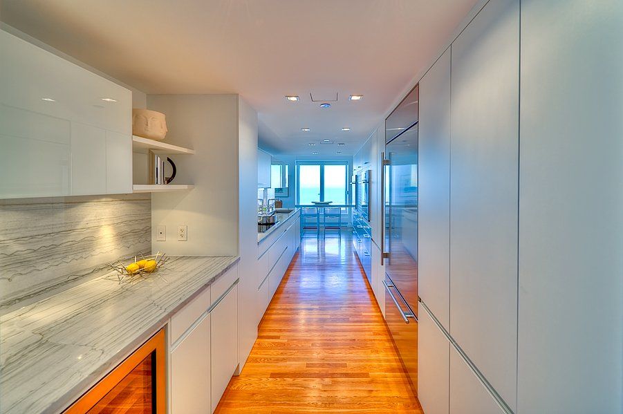 A long hallway in a kitchen with white cabinets and hardwood floors