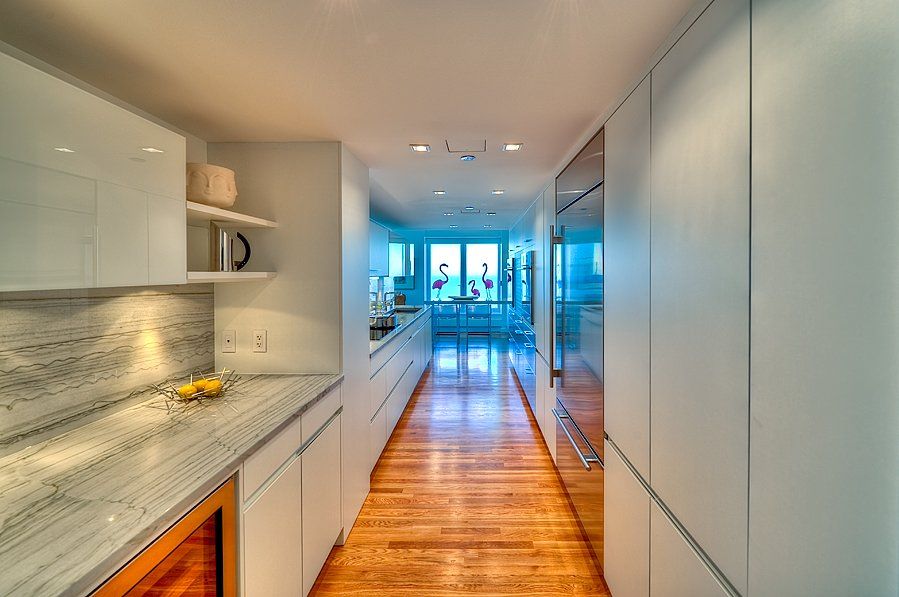 A long hallway in a kitchen with white cabinets and wooden floors