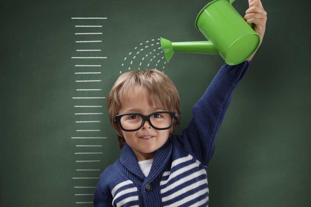 A young boy is holding a green watering can over his head.
