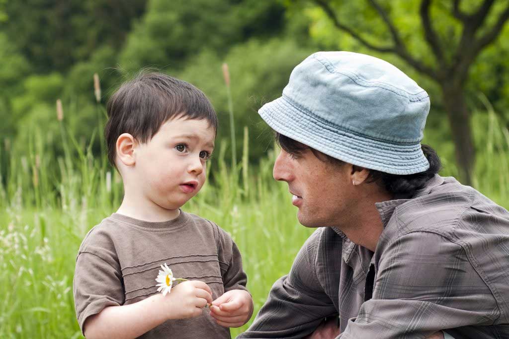 A man in a hat is talking to a little boy in a field.