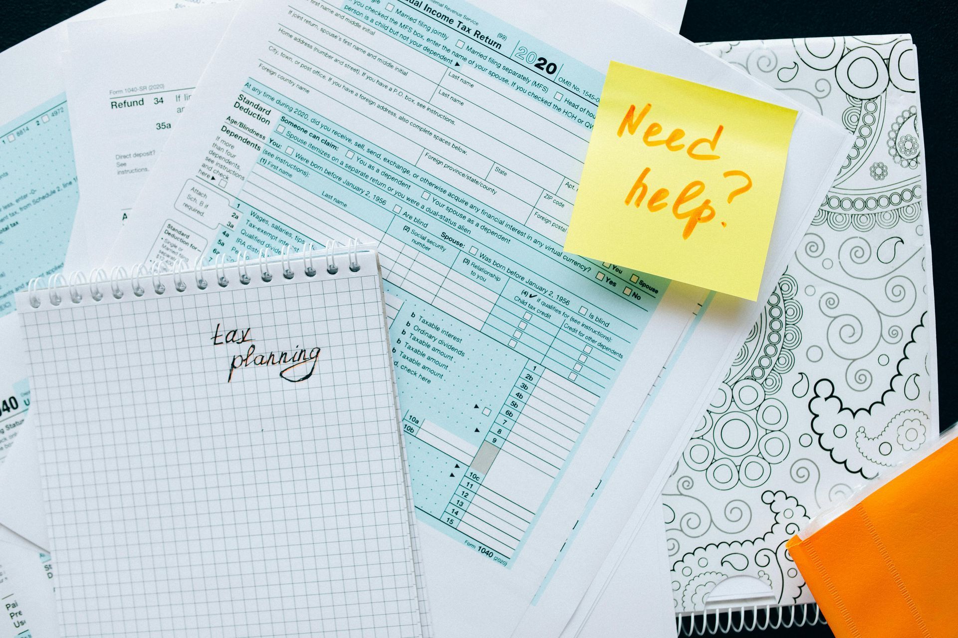 A yellow sticky note that says need help is sitting on top of a pile of papers.
