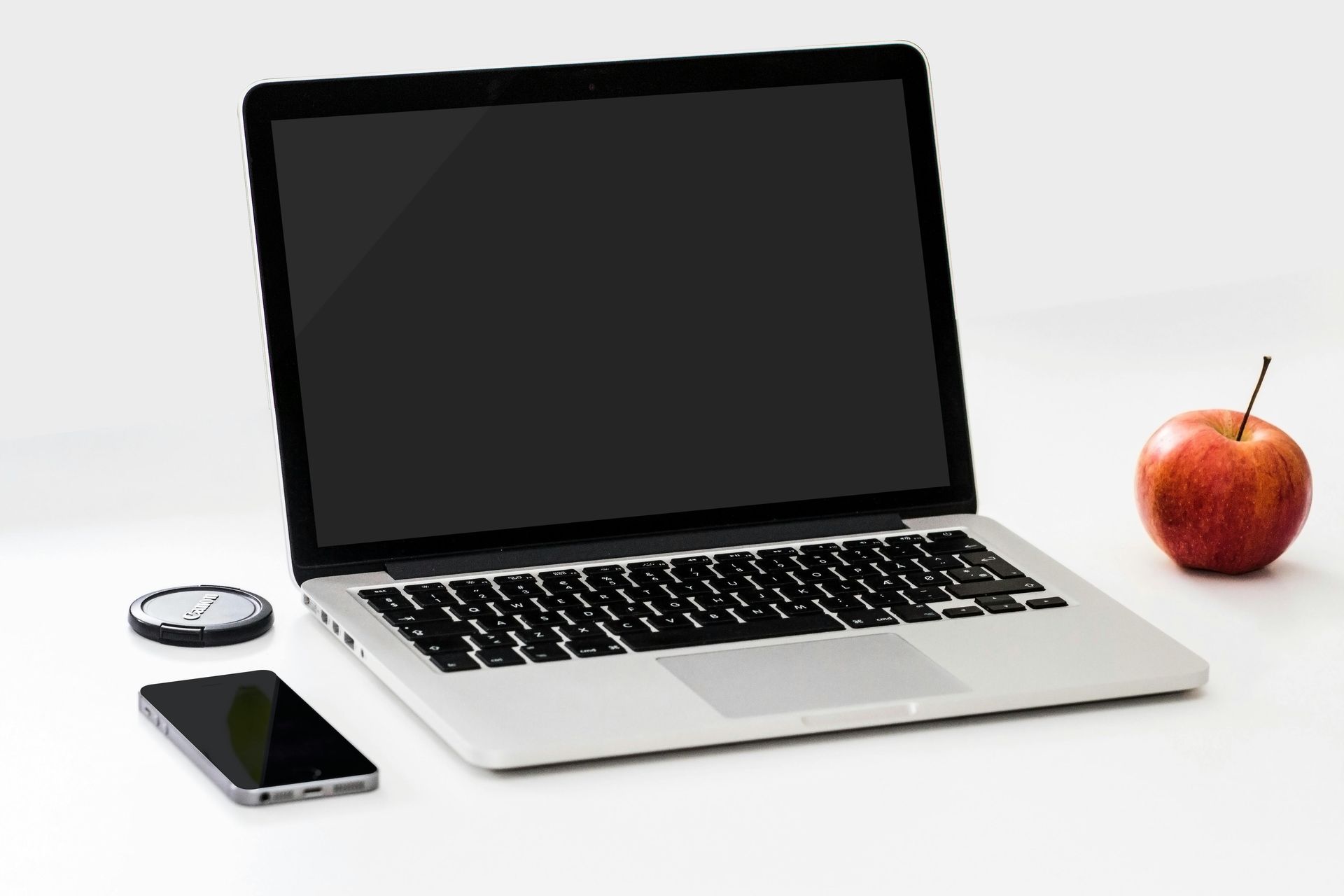 A laptop is open next to an apple and a cell phone