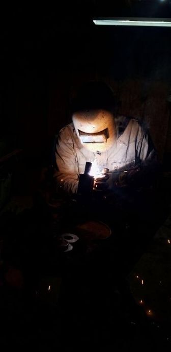 A man wearing a welding mask is grinding a piece of metal in a factory.