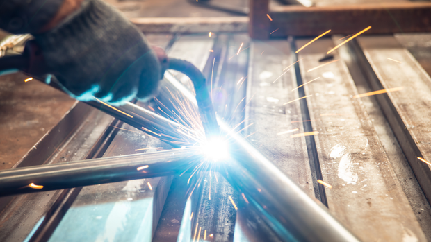 A person is welding a metal pipe in a factory.