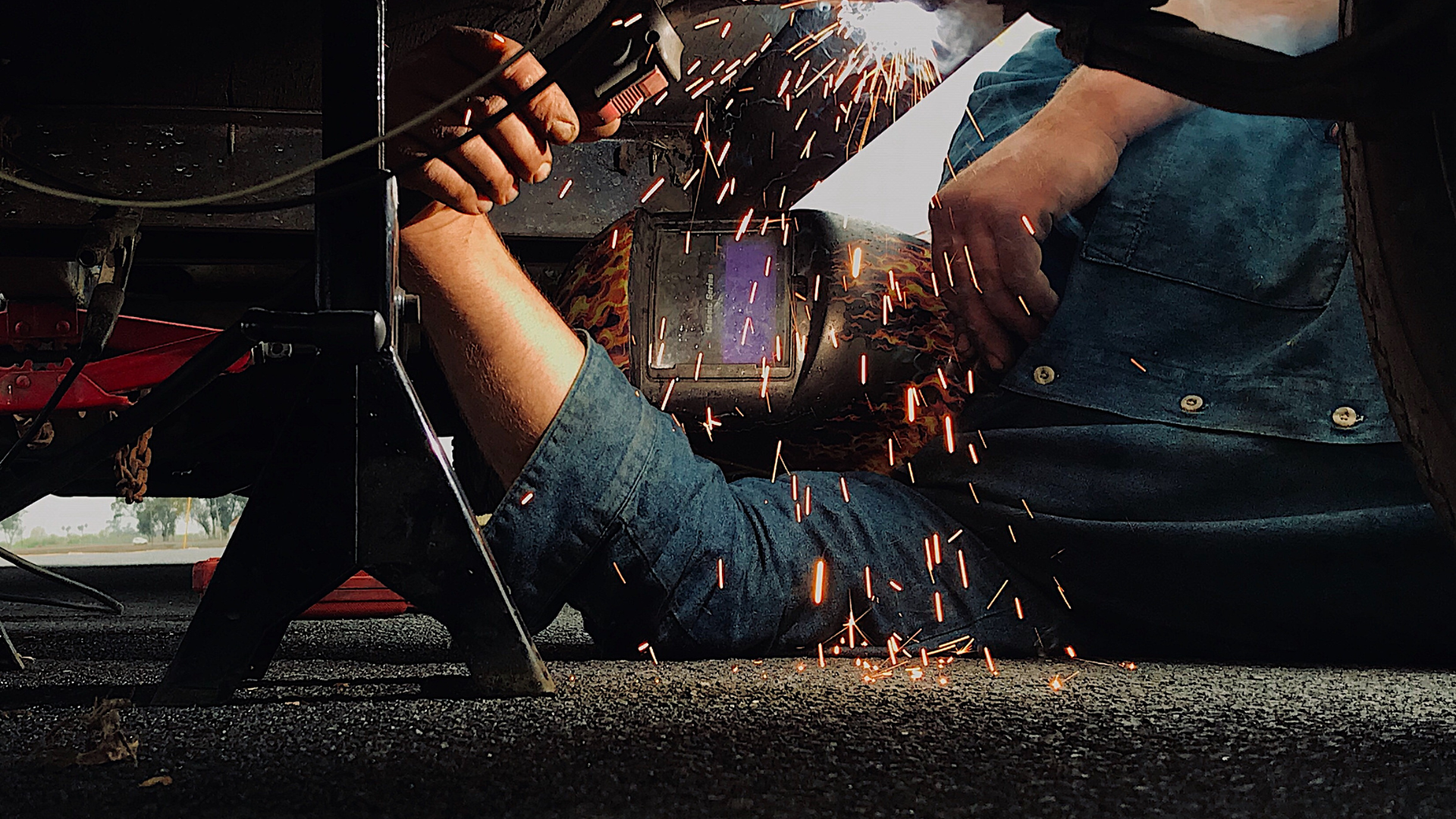 A man is welding a piece of metal under a car.